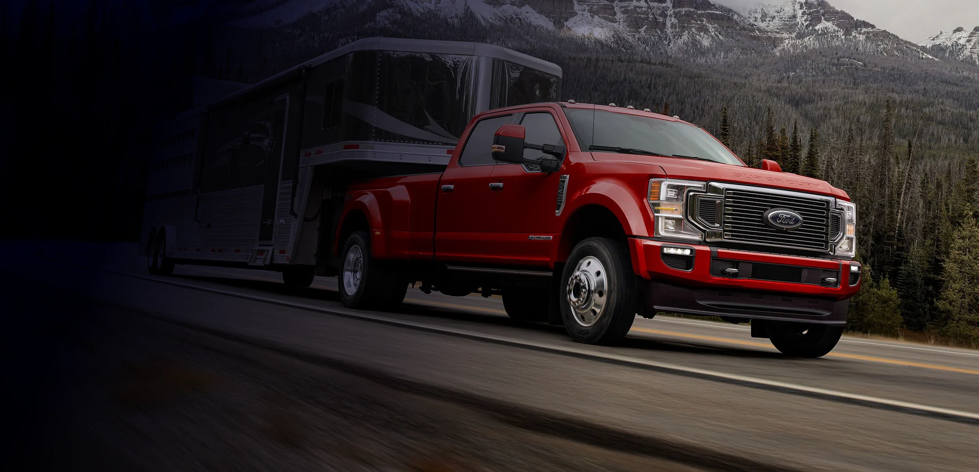 Red heavy-duty Ford truck towing a custom enclosed trailer on a mountain road